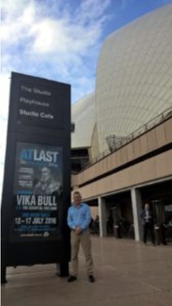 John Livings outside the Sydney Opera House beside the At Last poster